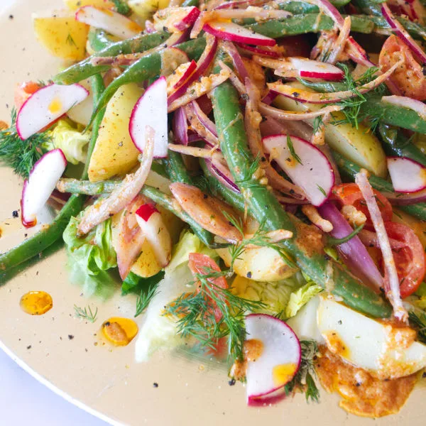 A platter of no-mayo potato salad is garnished with red onion and green beans.