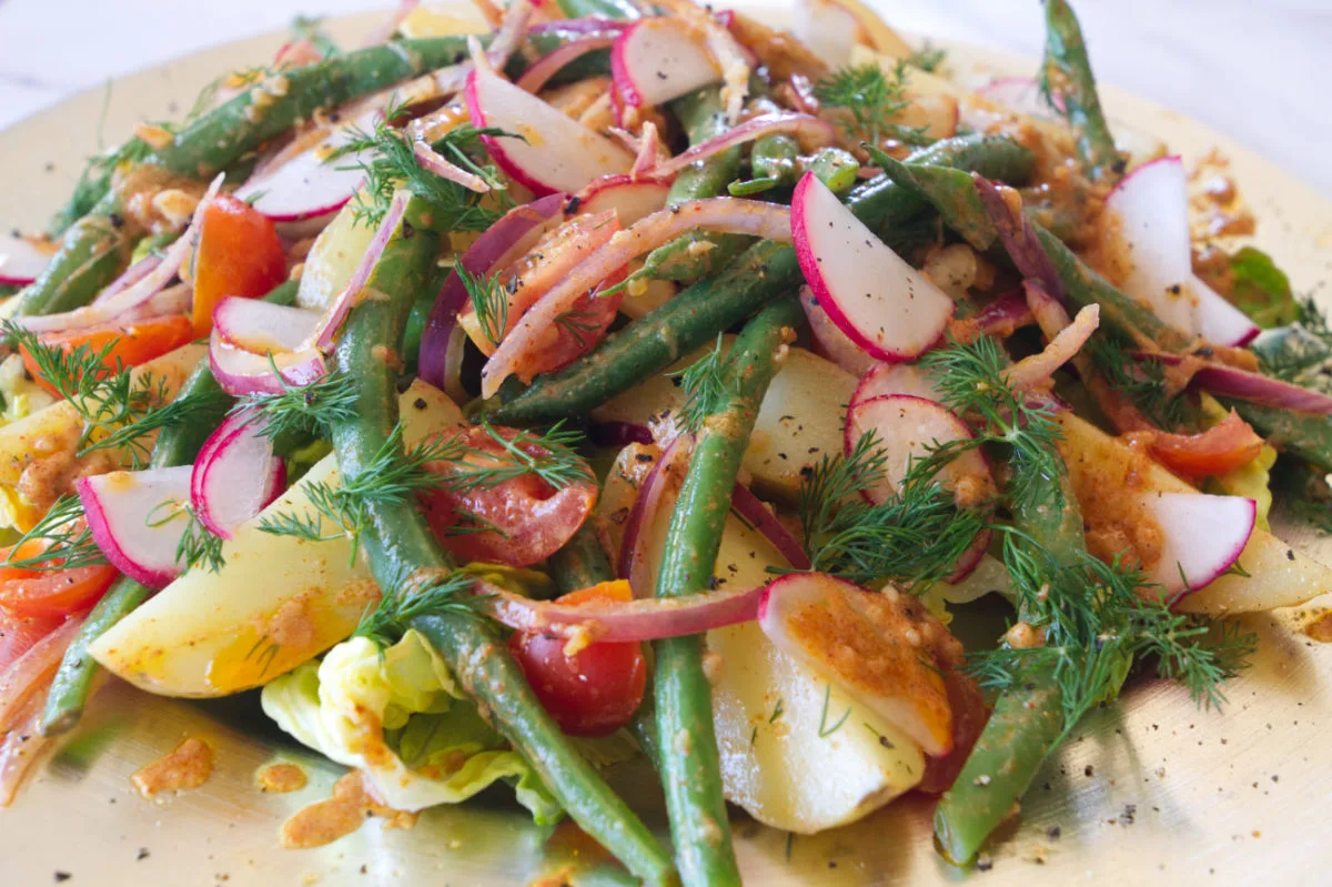 A platter of no-mayo potato salad is garnished with red onion and green beans.
