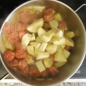 some potatoes are added to a pan with some fried chorizo and onions.
