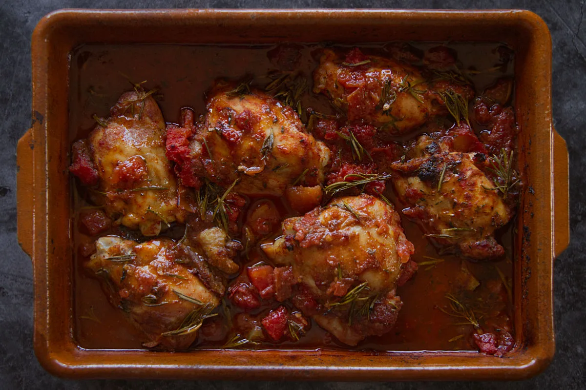 A pan of Roast chicken thighs cooked in a red wine, tomato, and herb sauce.