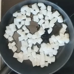 Squid cubes cook in a frying pan.