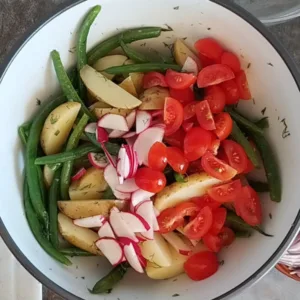 Some cherry ttomatoes, red onion, and radish are added to a bbowl with potatoes and green beans.