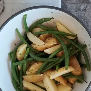 Wedges of potato and some green beansin a bowl with some dill.