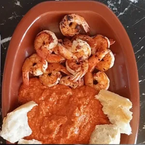 Some fresh bread pieces are added to a platter with pan-fried shrimp and romesco sauce.