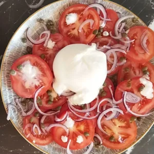 A ball of burrata cheese sits on top of a bed of sliced tomato and red onion.