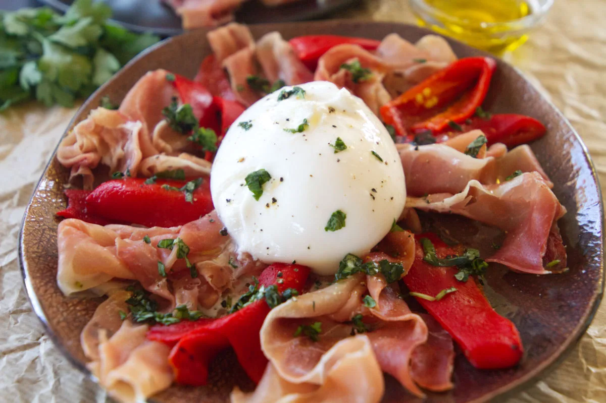 A plate of Burrata with serrano ham and roasted peppers.
