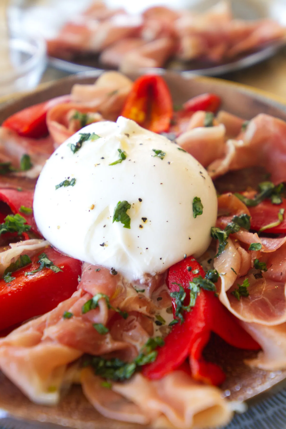 A plate of Burrata with serrano ham and roasted peppers.