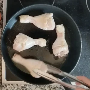 Some chicken drumsticks cook in a pan with some oil.