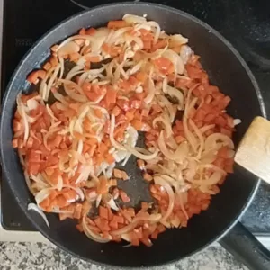Some red bell pepper is added to a pan with some sauteed onions.