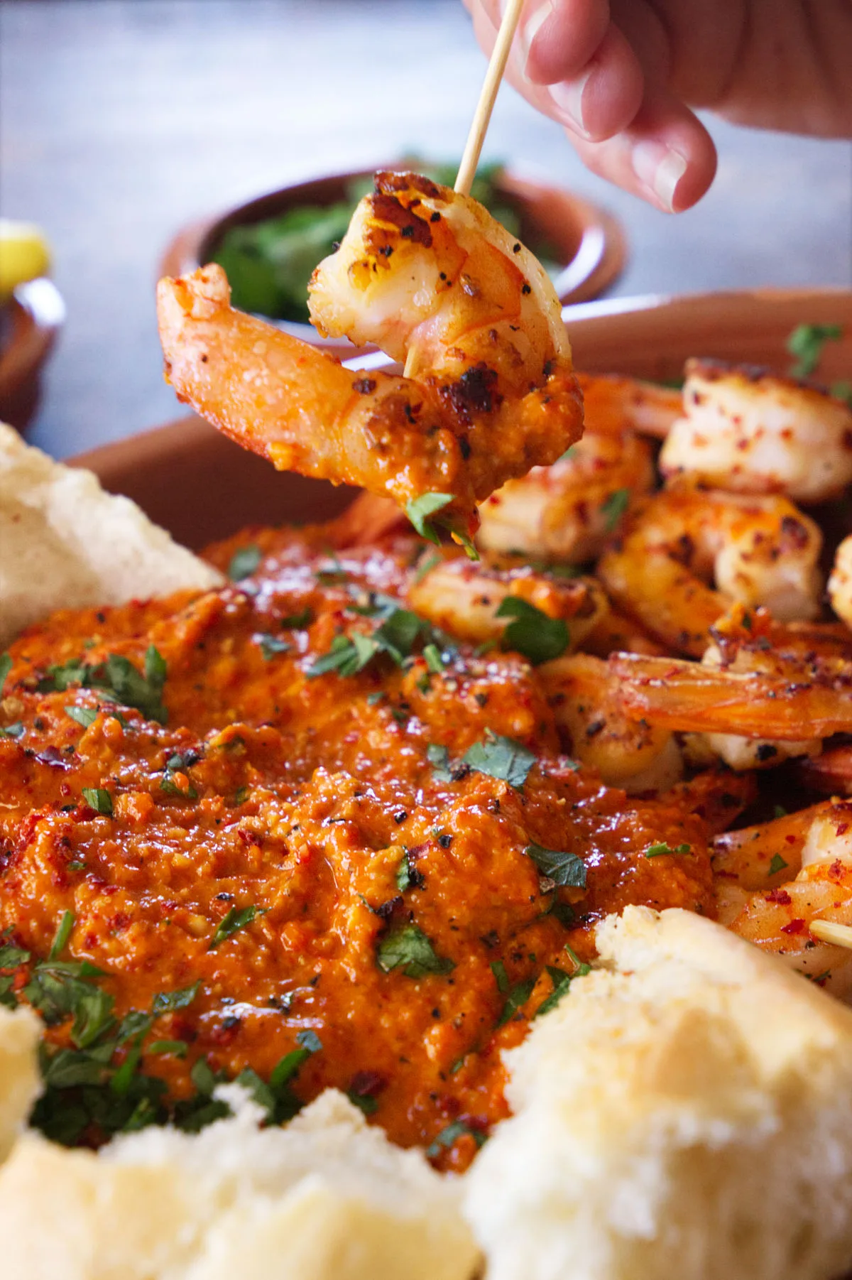 A shrimp on a skewer is dipped into some romesco sauce. 
