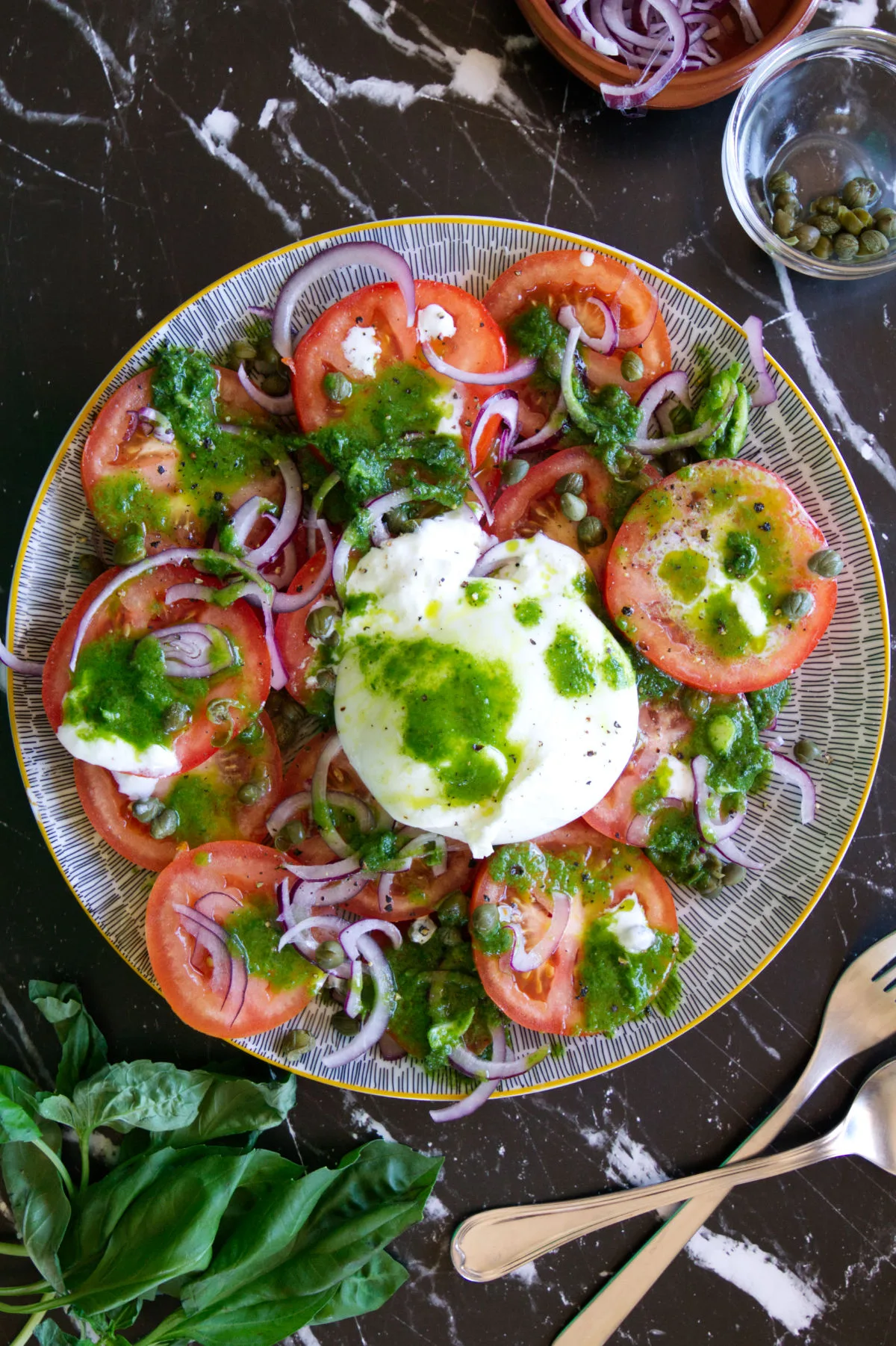 A plate of tomato burrata salad drizzled with a green basil and garlic dressing.