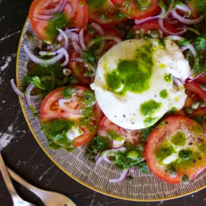A plate of tomato burrata salad drizzled with a green basil and garlic dressing.