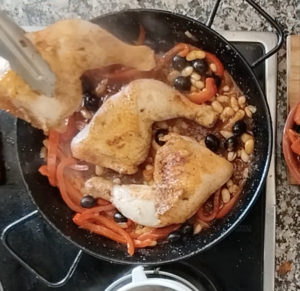 Browned chicken pieces are added to a pan with some simmered veggies.