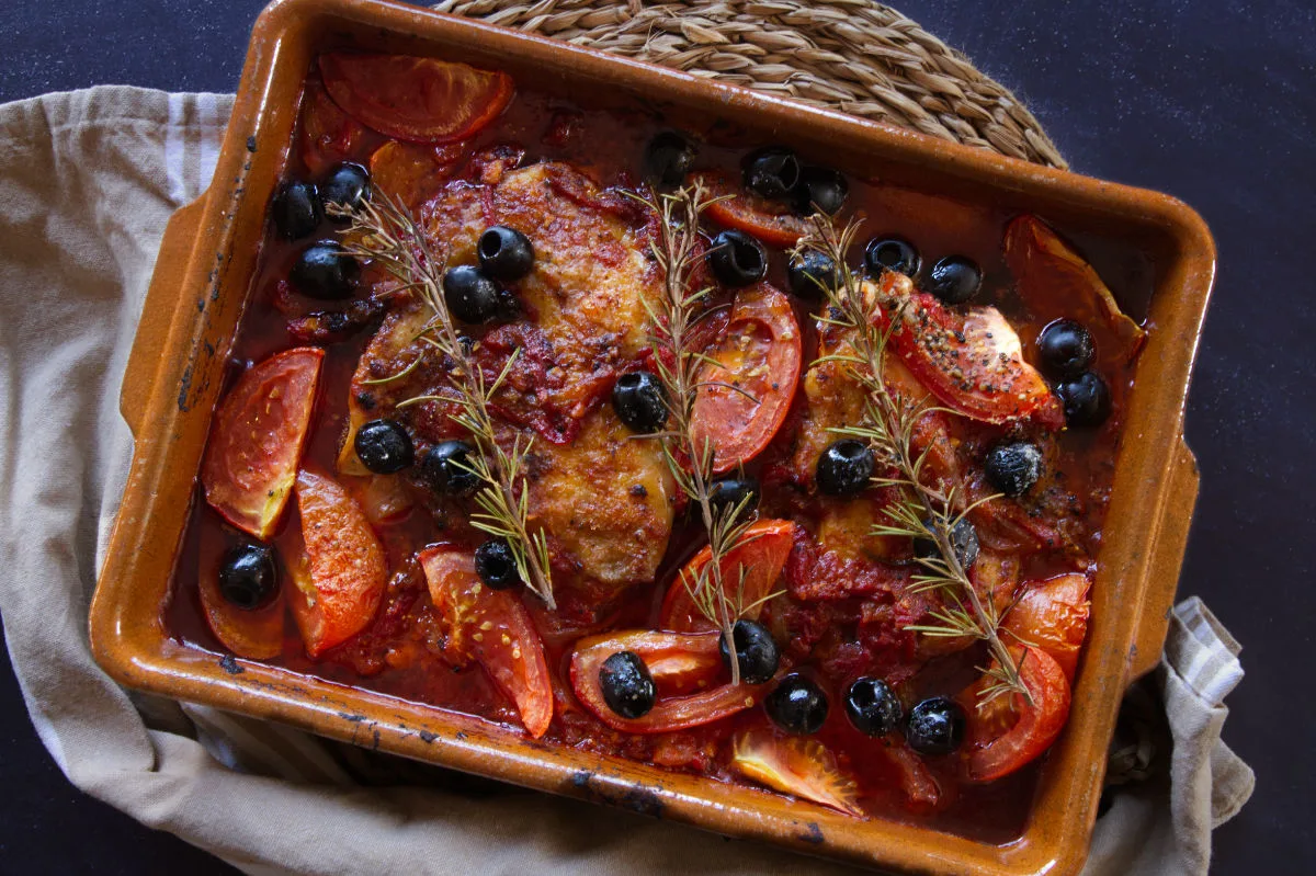 A large casserole dish of Mediterranean boneless chicken thighs with a rich red sofrito sauce.