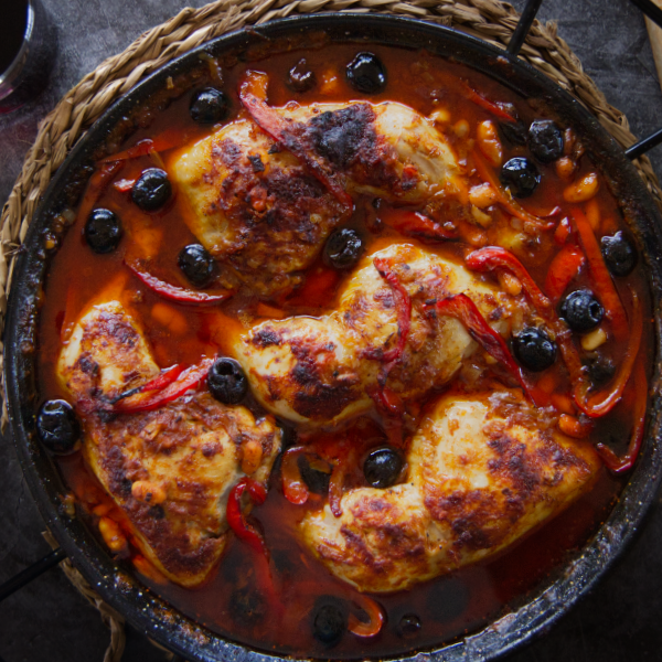 A pan of Spanish chicken with smoky Bravas sauce sits at a table setting.