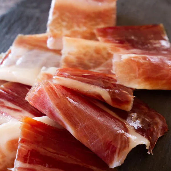 Slices of jamon iberico sit on a slate plate.