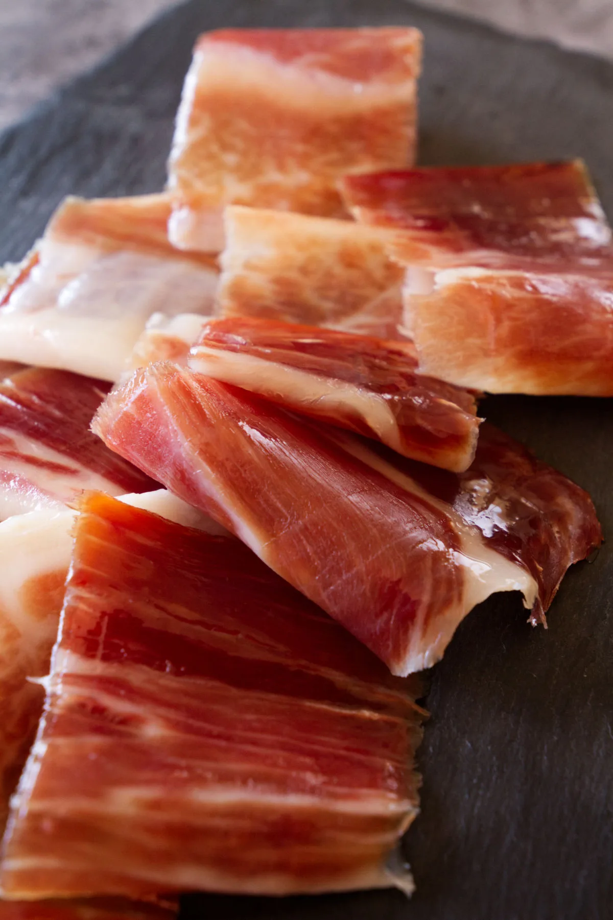 Slices of jamon iberico sit on a slate plate.