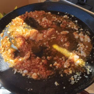 Sepia, tomato, paprika, and garlic are added to some onions in a large paella pan.
