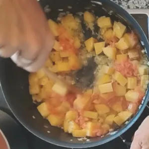 some grated tomatoes are added to the pot of onions and potatoes