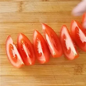 A tomato is cut into wedges on a chopping board.