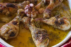 A dish of cooked chicken drumsticks with garlic and rosemary.