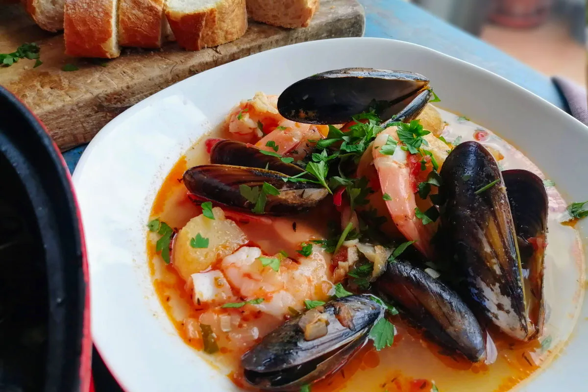 A bowl of seafood stew with giant mussels and shrimp, garnished with freshly chopped parsley.