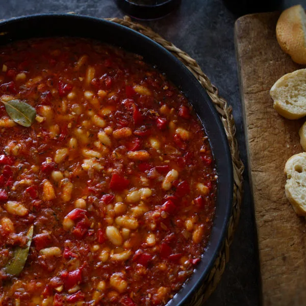 A large pan of Spanish-style white bean stew sits beside some sliced bread.
