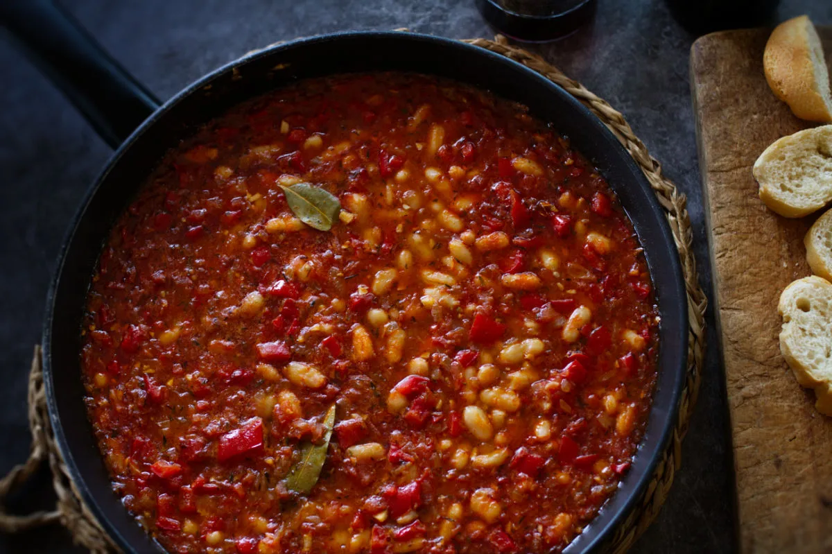 a large pan of white bean stew sits with a few bay leaves on top.