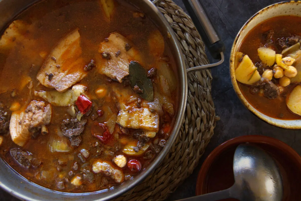 A large pot of spicy Spanish-style pork stew is served to a small bowl.