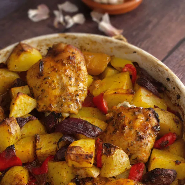 A large dish of cooked chicken thighs and roasted potatoes.