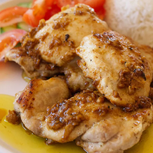 garlic-infused chicken thighs sit on a plate beside some steamed rice and salad.