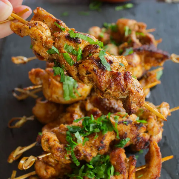 A small pile of paprika-infused chicken skewers sit on a slate plate.