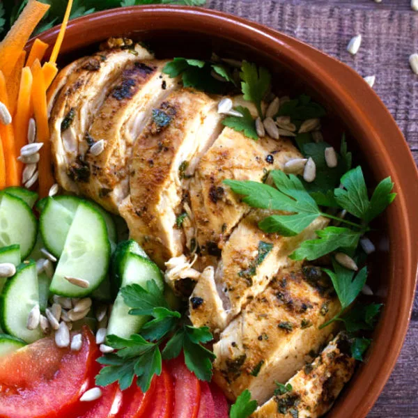 Slices of grilled Mediterranean chicken breast sit in a bowl with some salad.
