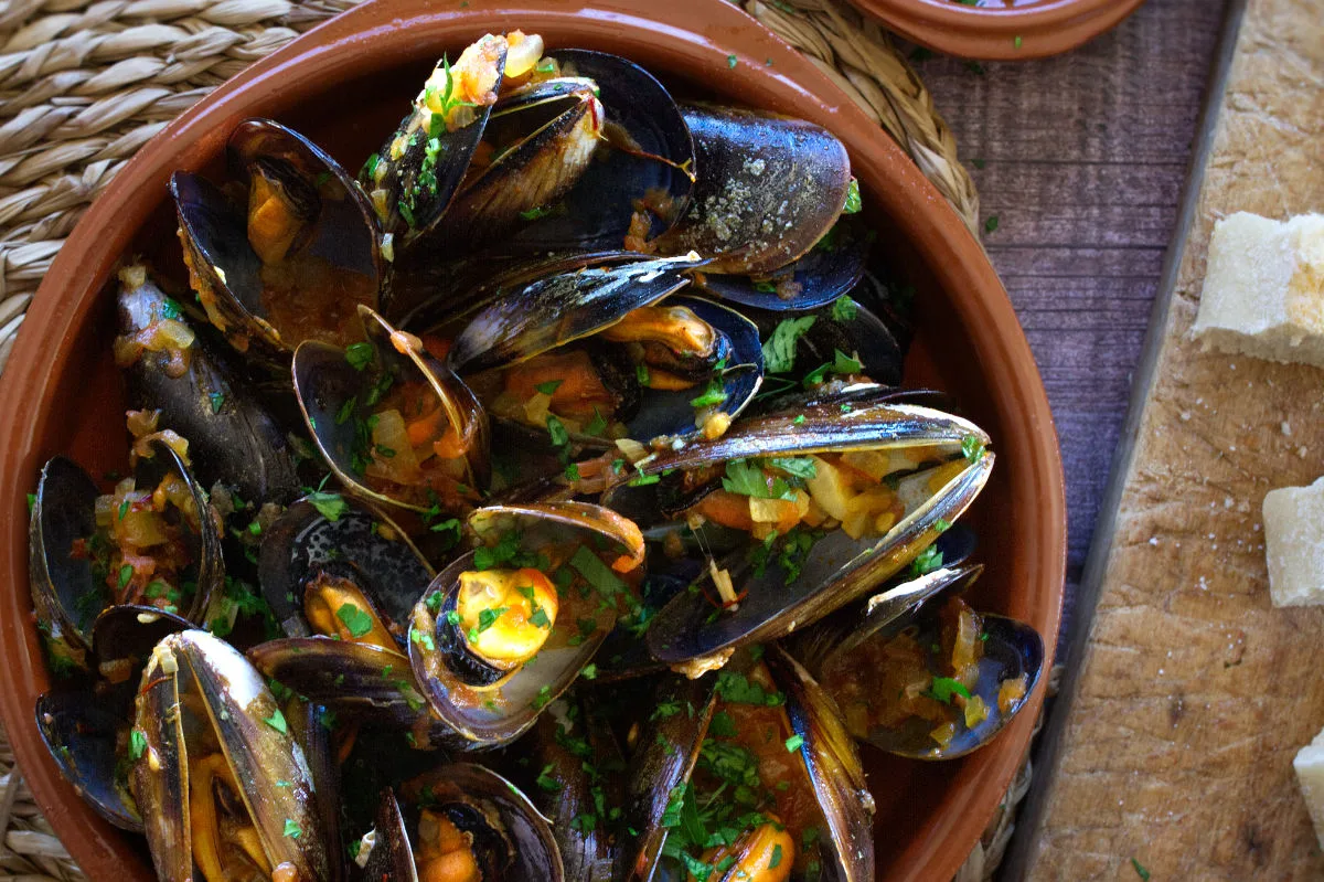 Spanish mussels in a rich tomato sofrito sauce sit in a bowl garnished with some fresh parsley.