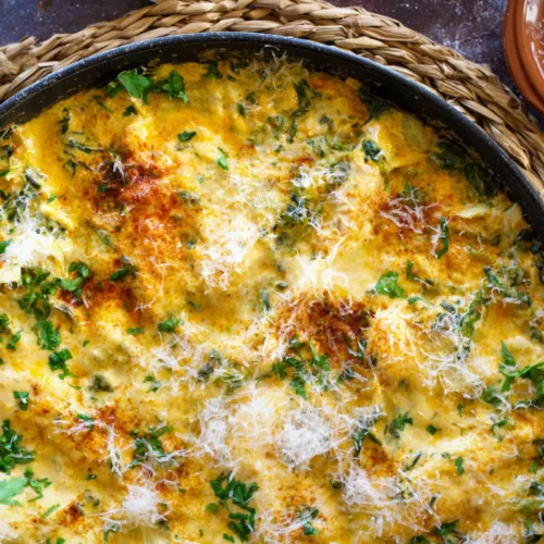 A large pan of creamy artichoke chicken with spinach and paprika.