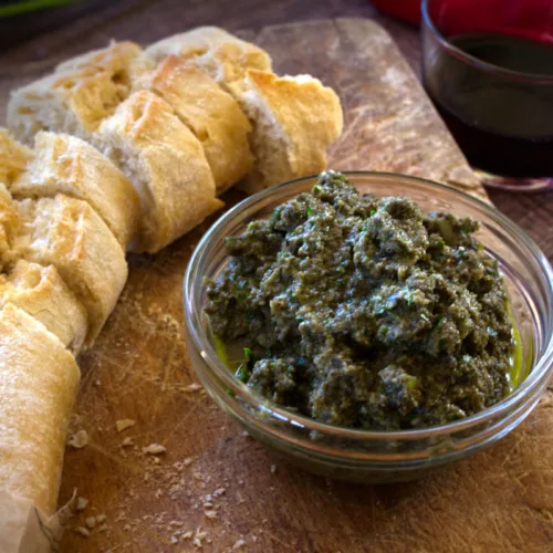 A small bowl of olive tapenade sits beside some sliced bread.