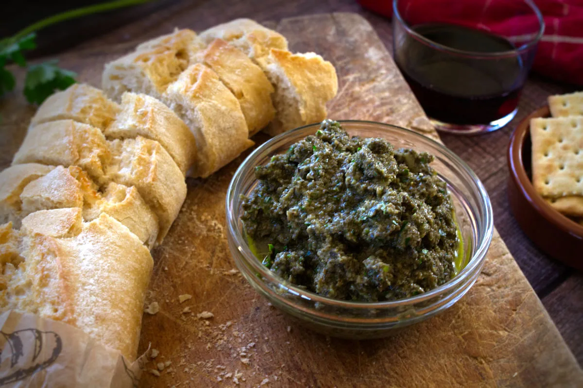 A small bowl of olive tapenade sits beside some sliced bread.