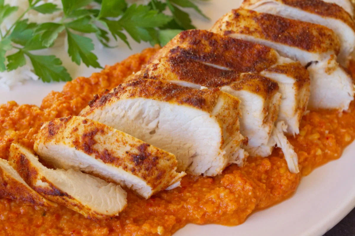 A plate fo sliced Roasted chicken breast with romesco sauce.