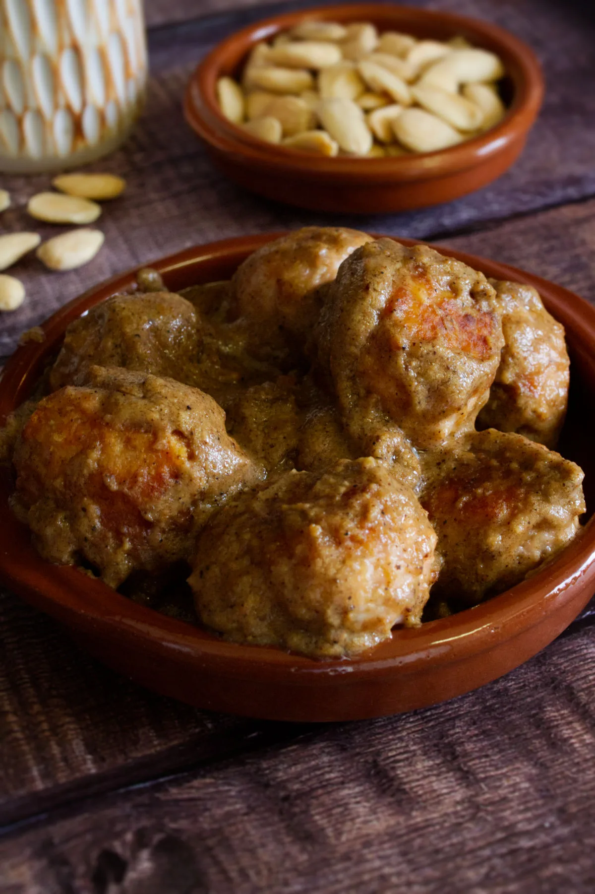 A small tapas serving of Chicken meatballs with almond sauce sits beside some amonds and aglass of red wine. 