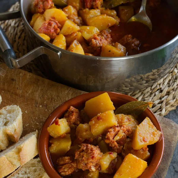 A large pot of Rioja-style potatoes with chorizo sits beside a small bowl serving.