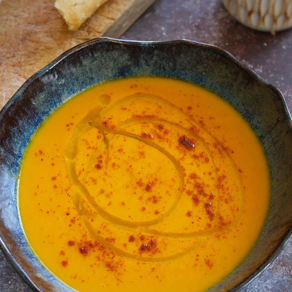 A bowl of spicy carrot soup sits beside some fresh bread.