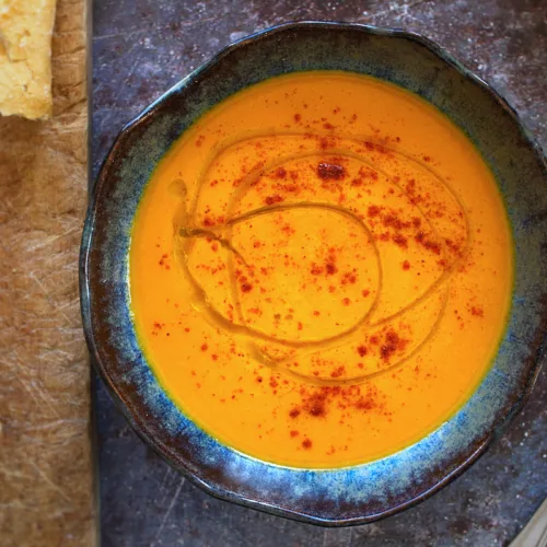 A bowl of carrot soup sits beside a large spoon.