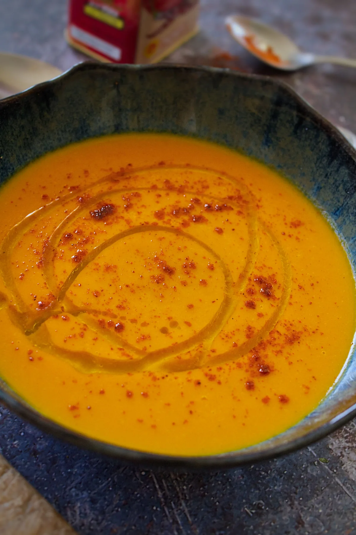 A bowl of spicy carrot soup sits beside some smoked paprika.