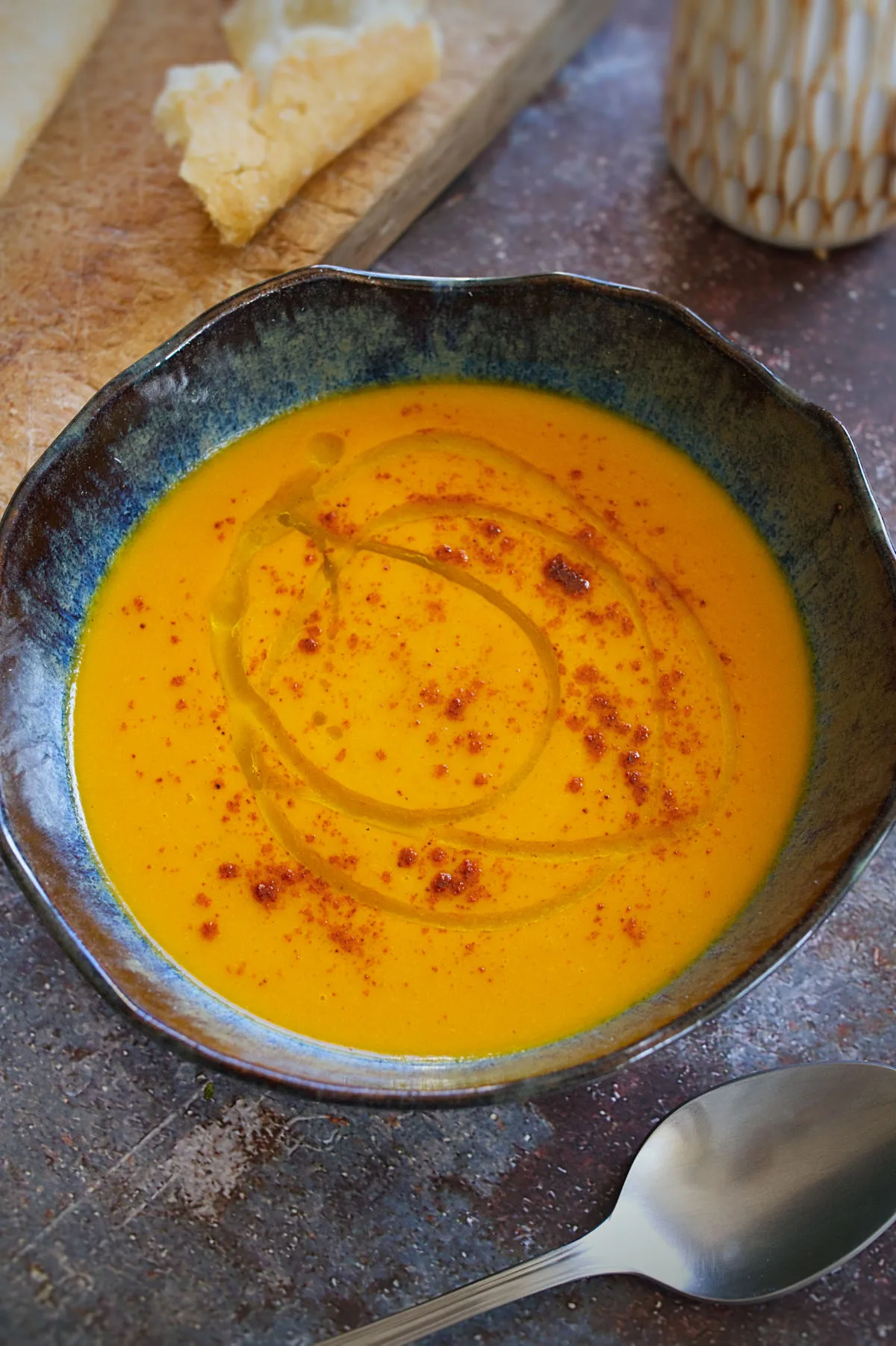 A bowl of spicy carrot soup sits beside some fresh bread. 