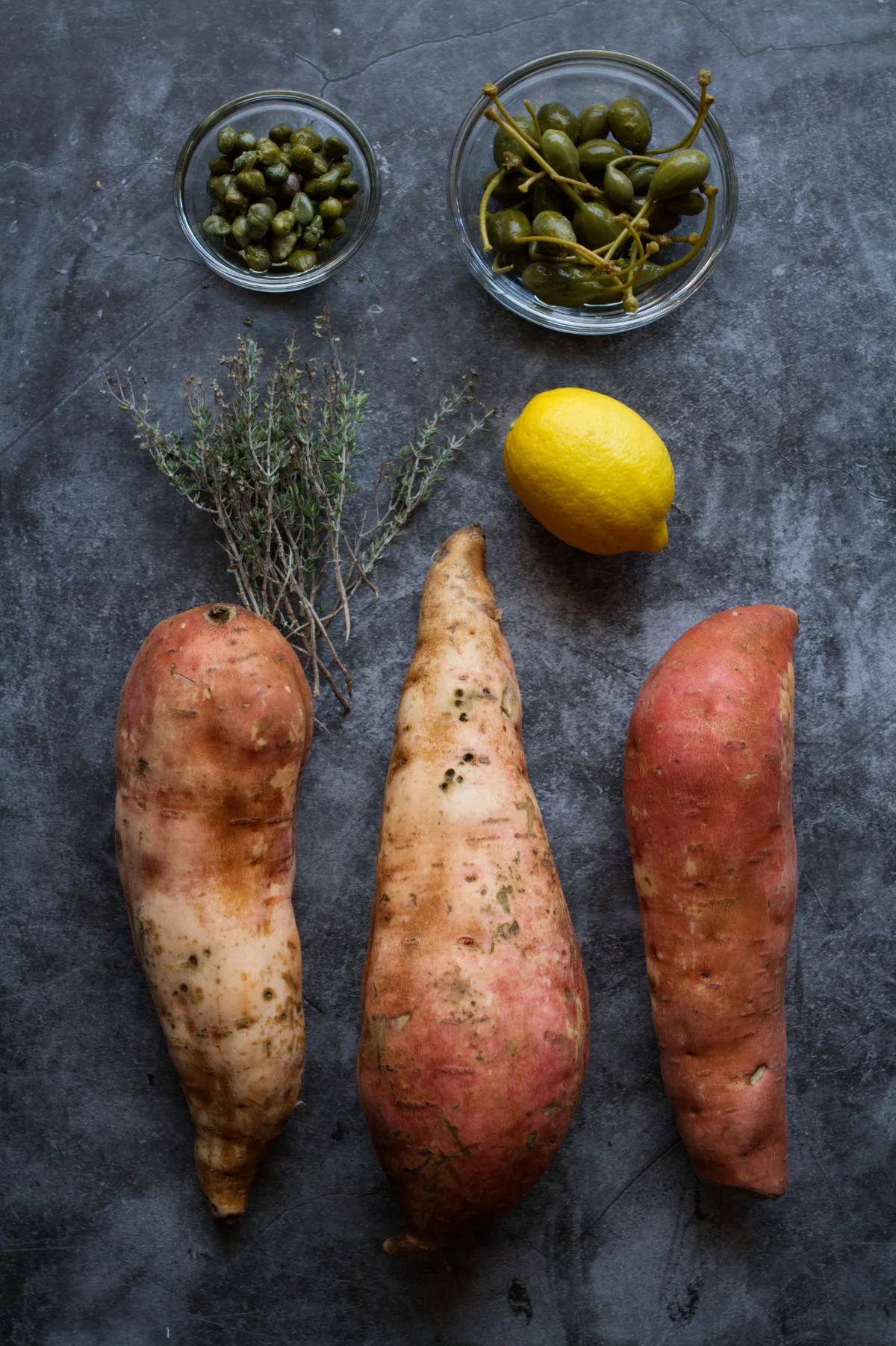 Sweet potatoes sit next to some lemon, fresh thyme, and capers.