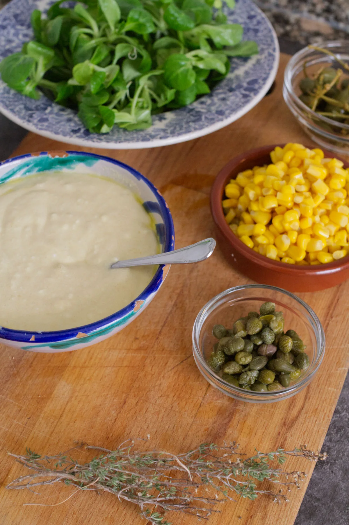 A bowl of yogurt dressing, sweet corn, letuce, and capers.