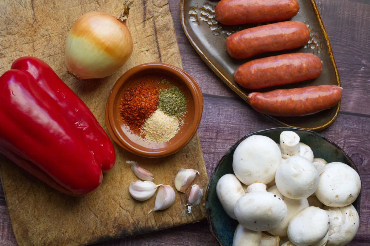 Chorizo sausages sit beside some button mushrooms, bell pepper, onion, garlic, and spices.