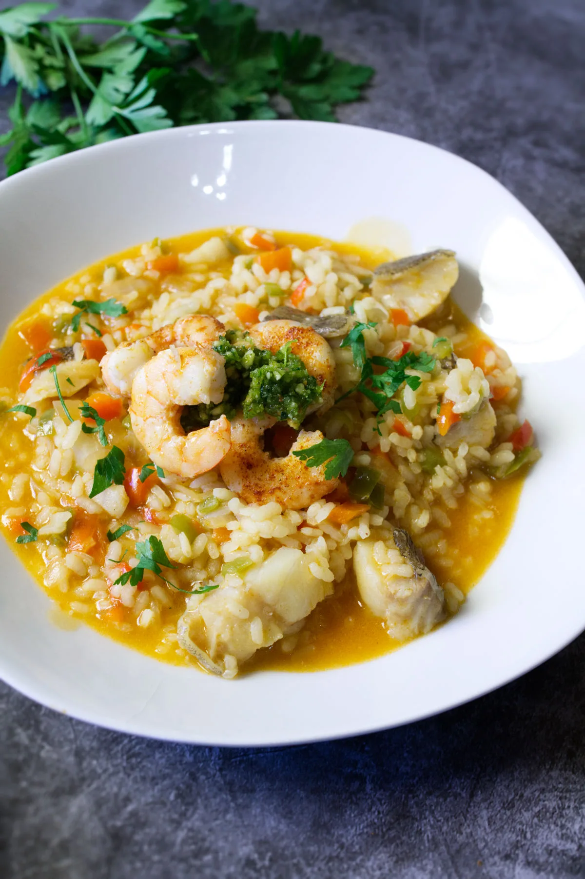 A bowl of brothy fish stew topped with some almond pesto and pan-fried shrimp.
