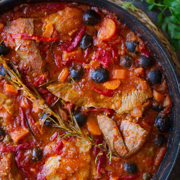 A large pan of Spanish pork secreto garnished with fresh roasemary and black olives.
