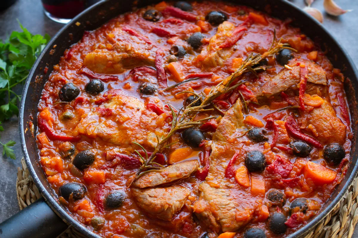 A alrge pan of Spanish pork secreto garnished with fresh roasemary and black olives.